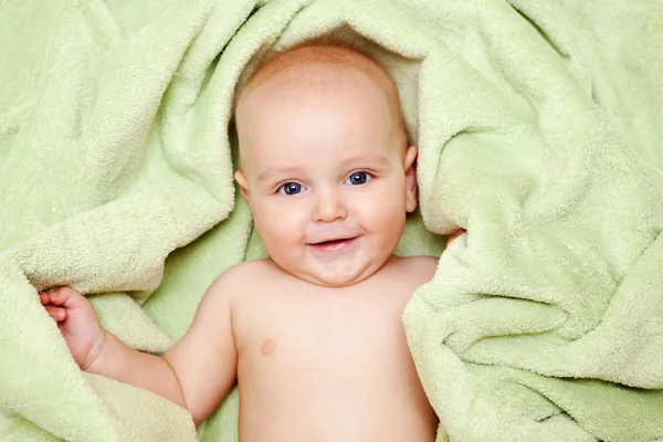 Caucasian baby boy covered with green towel joyfully smiles at c — Stock Photo, Image