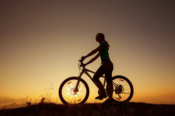 Biker-lány a naplementét a hegyek — Stock Fotó