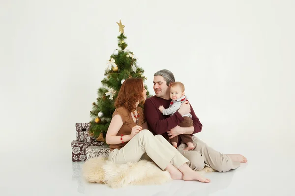 Šťastná rodina sedí na vánoční strom na bílém studio — Stock fotografie