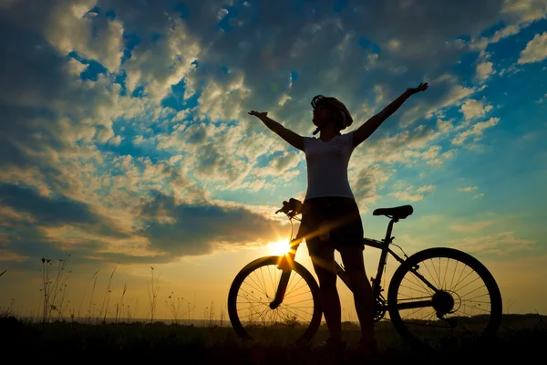 Ποδηλάτης-κορίτσι στο ηλιοβασίλεμα στο λιβάδι — Φωτογραφία Αρχείου