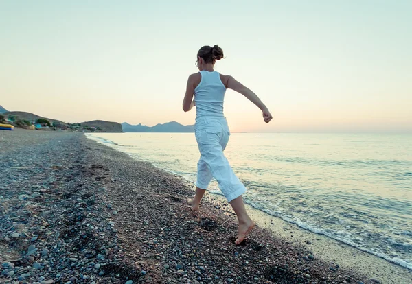 Vrouw doet ochtend oefeningen op de zee tijdens zonsopgang — Stockfoto