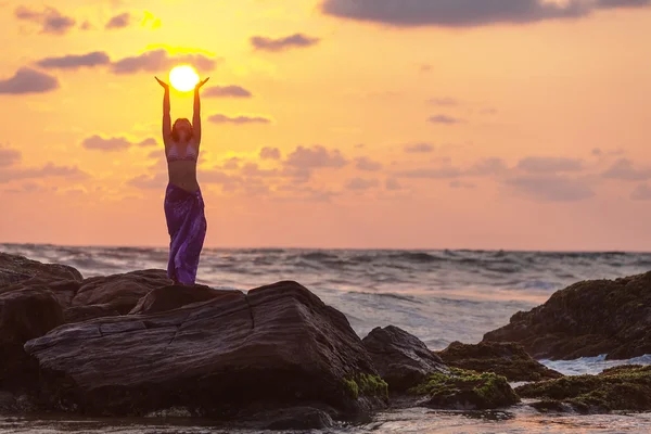 Woman stands at the rock and takes sunset sun in her hands