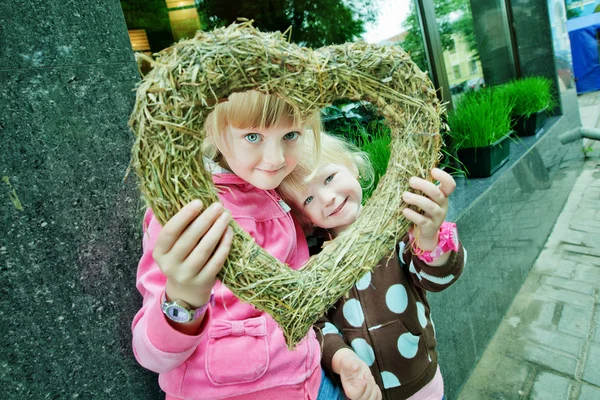 Två flickor titta igenom inredda hjärtat in i kameran — Stockfoto