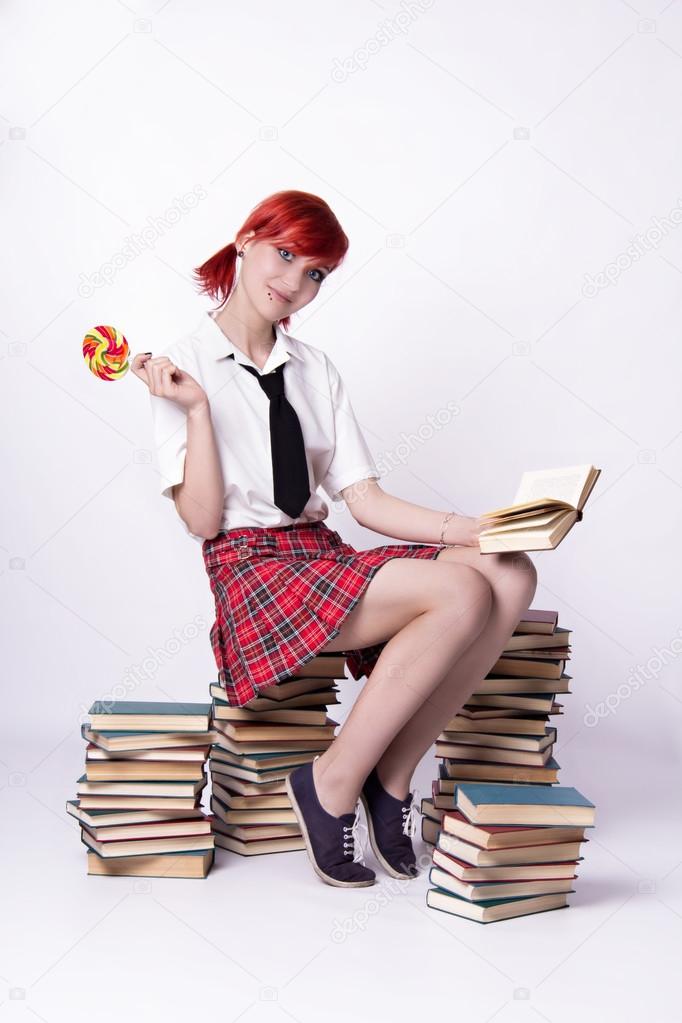 Girl with lollipop sitting on a pile of books