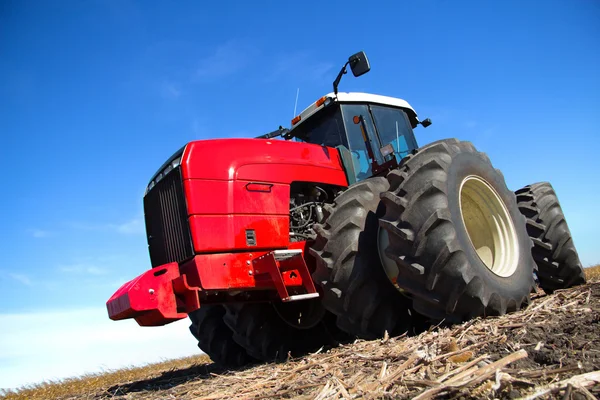 Красный трактор работает в поле — стоковое фото