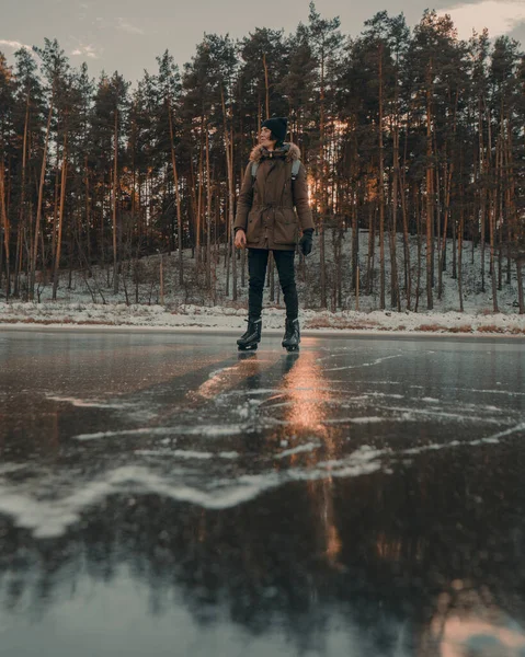 Buz patenli genç bir adam donmuş gölün buzunda duruyor.