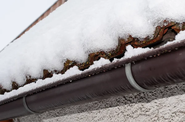 side view to the gutter and roof tiles of a house in winter covered with snow