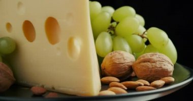 Orta boy sert peynirli Edam gouda parmesan peynirinin bir kısmını ahşap tahtada, fındık ve üzümler tabakta dönüyor..