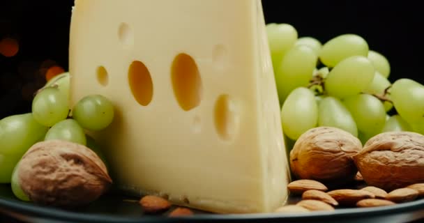 Närbild del av Medium hårdost huvud edam gouda parmesan på träskiva, med nötter och druvor rotaiting på plattan. — Stockvideo