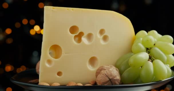 Fechar parte da cabeça de queijo duro médio edam gouda parmesão em tábua de madeira, com nozes e uvas rotaiting no prato. — Vídeo de Stock