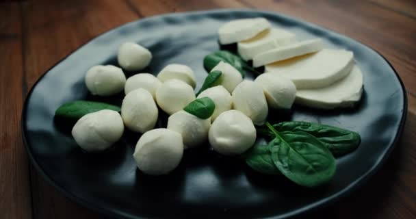 Witte kleine mozzarella kaasballen, spinazie bladeren op zwarte plaat. Dolly-in schot. — Stockvideo