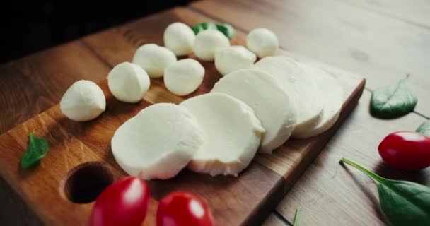 Petites boules de fromage mozzarella blanches, feuilles d'épinards sur planche de bois. Prise de vue Dolly-in. — Video