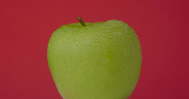 Pomme verte humide tourne suspendue sur un fond rouge, isolée. — Video