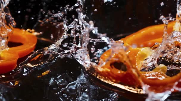 Rodajas de pimiento de orandge caen sobre tabla de madera marrón con gotas de agua. — Vídeo de stock