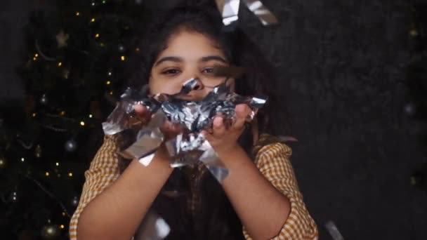 Feliz chica africana celebrando la Navidad. Joven adolescente soplando en confeti cerca de un árbol de Año Nuevo. — Vídeo de stock