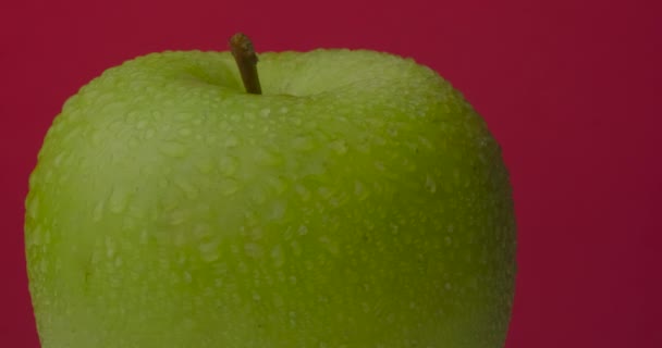 Pomme verte humide tourne suspendue sur un fond rouge, isolée. — Video