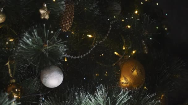 In der Nähe leuchtet ein Weihnachtsbaum, der nachts glitzert. Neujahrstanne mit Dekoration und Beleuchtung. Weihnachtsbaumschmuck Hintergrund. Viele große goldene Kugeln an Tannenbaum Neujahr und Weihnachten. — Stockvideo