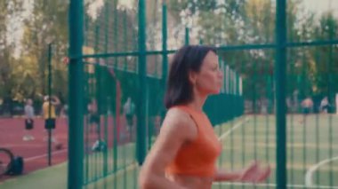 Turuncu spor kıyafetleriyle koşan beyaz kadın spor sahasında kardiyo antrenmanı yapıyor..