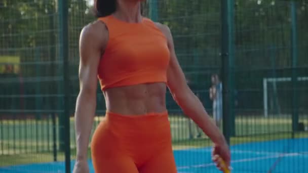 Mladá fit fena v oranžovém sportovním oblečení dělá skok cvičení na sportovním hřišti s skákacím lanem. — Stock video