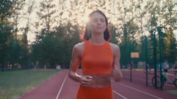 Vista frontal de la mujer caucásica corriendo en ropa deportiva naranja haciendo ejercicio cardiovascular en el campo de deportes. — Vídeo de stock