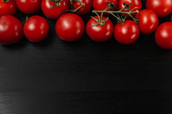 Koyu arkaplanda yeşil yapraklı kırmızı domatesler