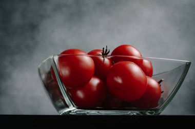 Yeşil yapraklı kırmızı domatesler gri arka planda cam kasede. Organik sağlıklı yiyecekler. Çiğ domates. Taze sebze.