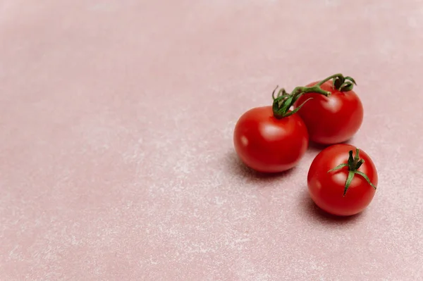 Pembe arka planda yeşil yapraklı kırmızı domatesler. Organik sağlıklı yiyecekler. Çiğ domates. Taze sebze.