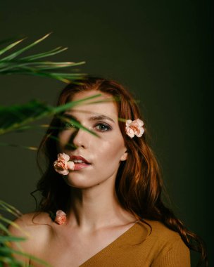 Ağzında çiçekle koyu yeşil arka planda poz veren güzel kızıl saçlı kız.