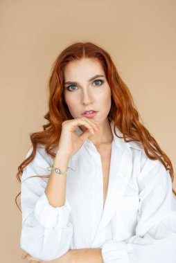 Beyaz tişörtlü, şeftali rengi arka planda poz veren güzel kızıl saçlı kız.