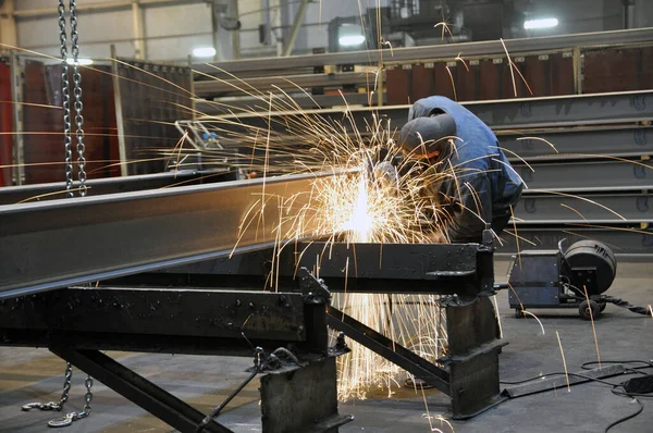 A worker in a factory is cleaning the steel structure of an angle grinder in a workshop. Sparks