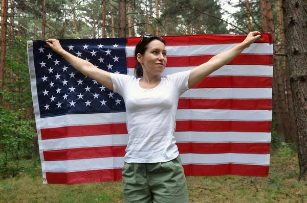 Jonge Amerikaanse vrouw met een Amerikaanse vlag op een bosachtergrond. — Stockfoto