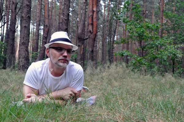 Junger Mann mit Hut und Wald, auf dem Boden im Wald liegend, das Leben genießend. — Stockfoto