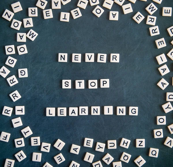 never stop learning phrase written on grey chalkboard background with frame of scattered letters. Square instagram format, flat lay top view