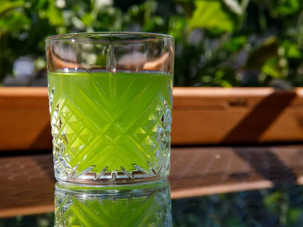 Glass with a bright green chilled drink on the table in a street outside cafe with a view of the sea in the sun day. Horizontal, copy space, side view