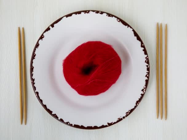 用木制双尖针头在白盘上打一个有趣的纱球 编织作为业余爱好 瓷盘上的红色马海毛毛线球 顶部视图 水平画面 当代艺术概念 — 图库视频影像