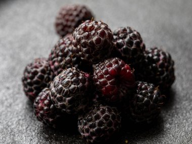 Taze böğürtlen yığını, yakın çekim. Siyah arka planda bir sürü olgun, sulu yabani meyve var. Üst Manzara Düz Yat