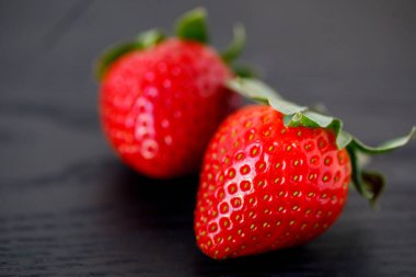 Yakın çekim ve yan görüş, iki büyük kırmızı çilek ahşap siyah zemin üzerinde, yatay, kopyalama alanı