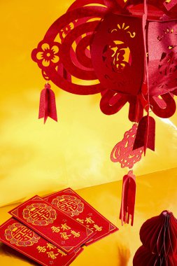 Sarı arka planda altın harflerle süslenmiş kırmızı bir angpao, kağıt fener ve kurdele. Çin Yeni Yılı için uygun, kutlama, zenginlik, refah ve kültürel tasarım kavramları.