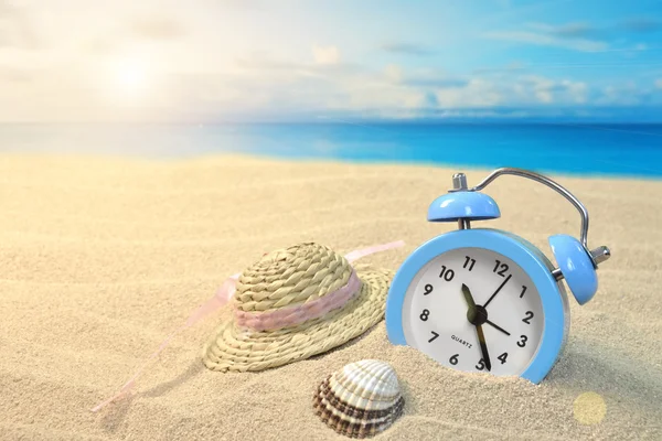 Relógio despertador e chapéu na praia — Fotografia de Stock