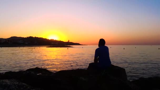 Чоловік сидить серед скель, спостерігаючи за сходом сонця — стокове відео