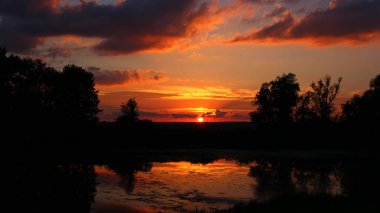 Gün batımında doymuş kırmızı gökyüzü, nehir ve bulutlarla manzaralı manzara