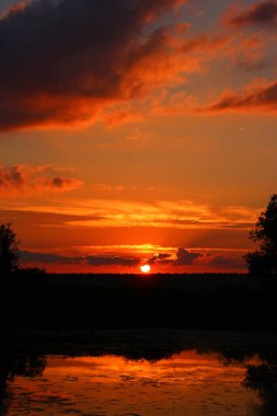 Gün batımında doymuş kırmızı gökyüzü, nehir ve bulutlarla manzaralı manzara