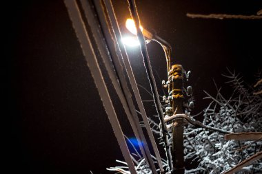 Geceleri sokak lambasının altında kar ve kablolar var.