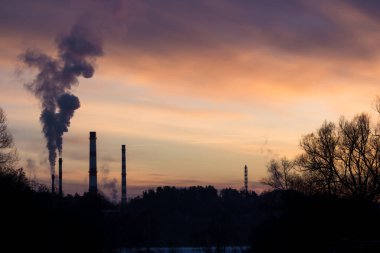 Sigara içilen boruların arkasında renkli bir günbatımı. Günbatımında sanayi manzarası