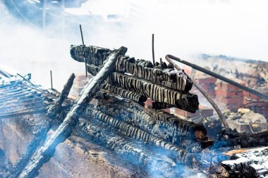 Yanmış tahtalar ve küllerde duman, yangından sonra yanan ahşap bir evin duvarları.