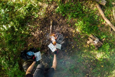 Kamp ateşinde kağıt yakan bir adam.