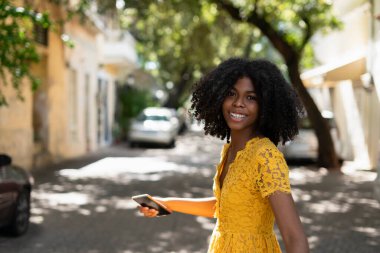 Young black woman with curly hair, in yellow dress and with styles, attitude, laughing, happy