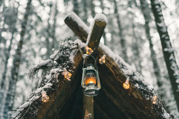 Lámpara de queroseno y guirnaldas colgando de refugio de supervivencia en bosque de invierno —  Fotos de Stock