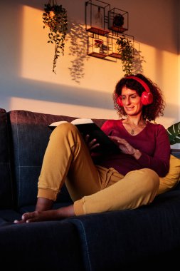 Coronavirus karantinası sırasında kanepede kitap okuyan bir kadın. Ev konseptine bağlı kal.