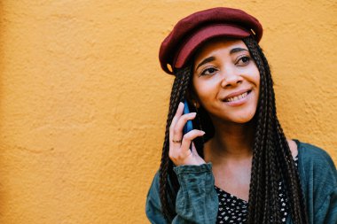 Örgülü siyah kadın akıllı telefonuyla telefon görüşmesi yapıyor.